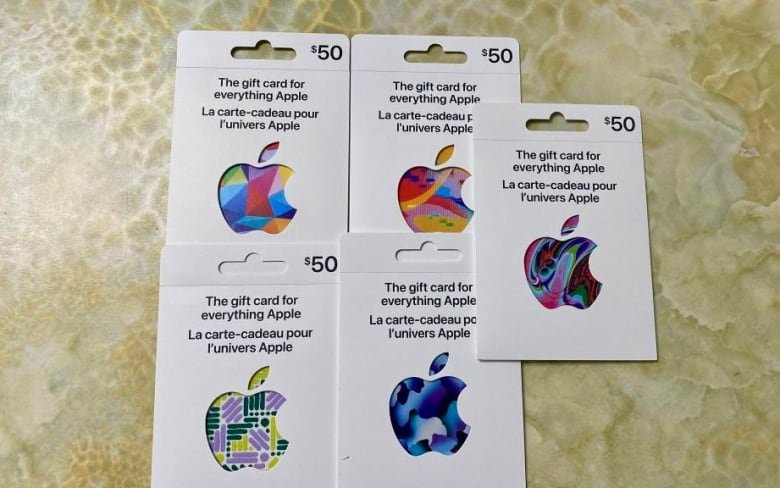 Five white $50 gift cards lay on a tiled surface. Each one has a multi-coloured Apple logo on it.