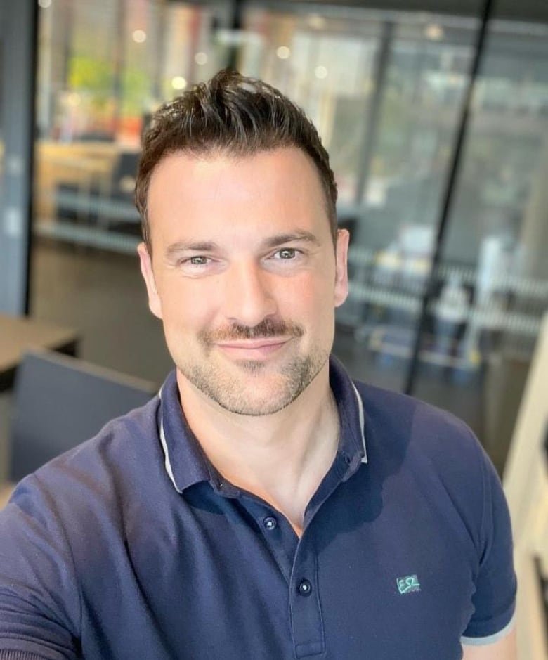 A white middle-aged man in a dark blue polo shirt with short brown hair smiles for a selfie.