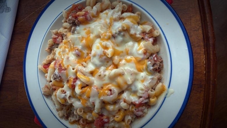 A big bowl of melted marble cheese on top of macaroni noodles with tomato sauce and ground beef.