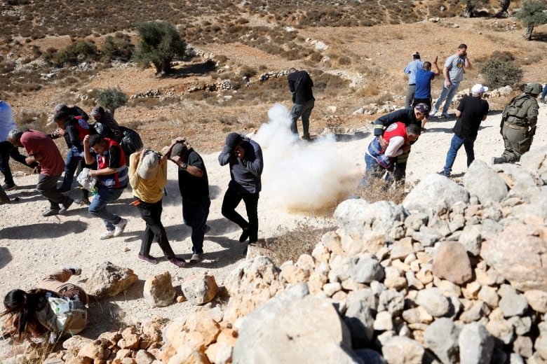 Palestinians run for cover from a stun grenade as Israeli troops deny access to farmers to harvest olives, in Burqa near Ramallah in the Israeli-occupied West Bank October 20, 2024.