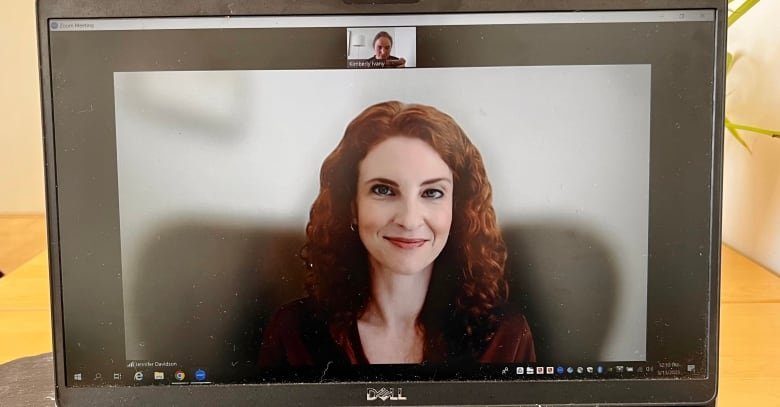 A smiling woman with red curly hair is seen a laptop screen.