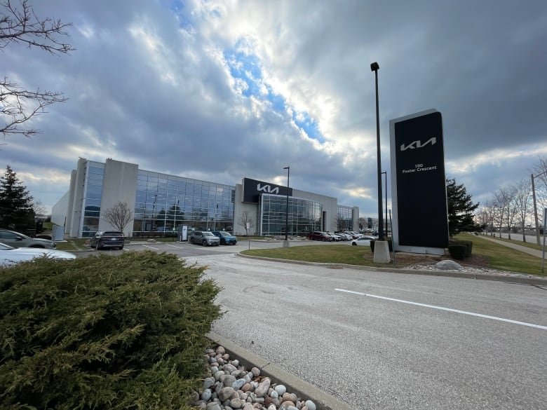 A wide-shot of a building with a large wall of windows. Kia Canada's logo is on the building, and on a sign post in front of the building.