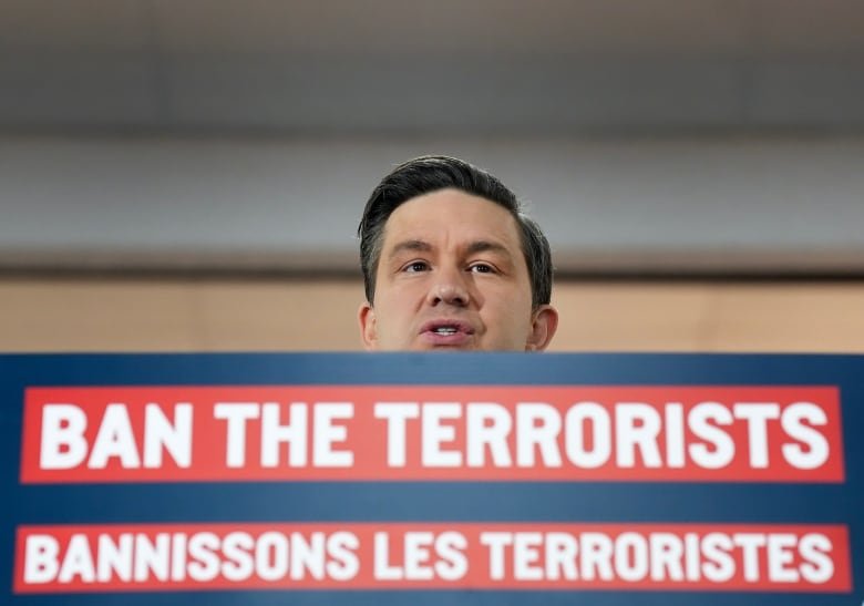 Conservative Leader Pierre Poilievre stands at a podium, his face is visible above a bilingual sign that says "ban the terrorists."