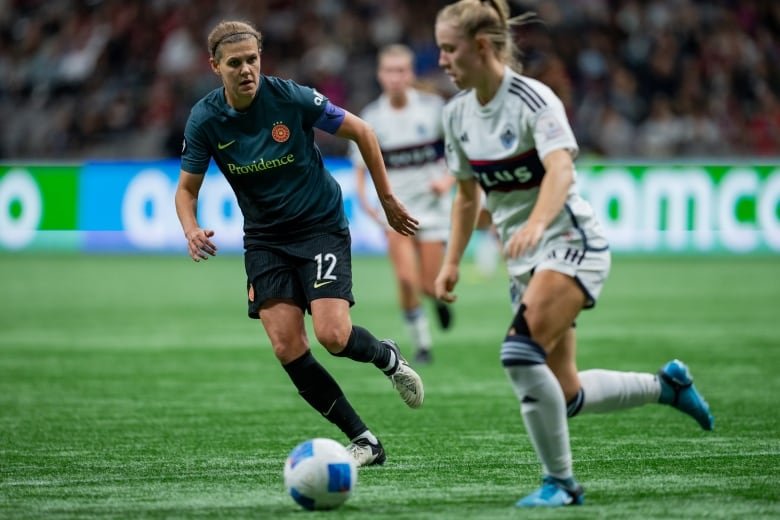 Two soccer players go after a ball on the pitch.