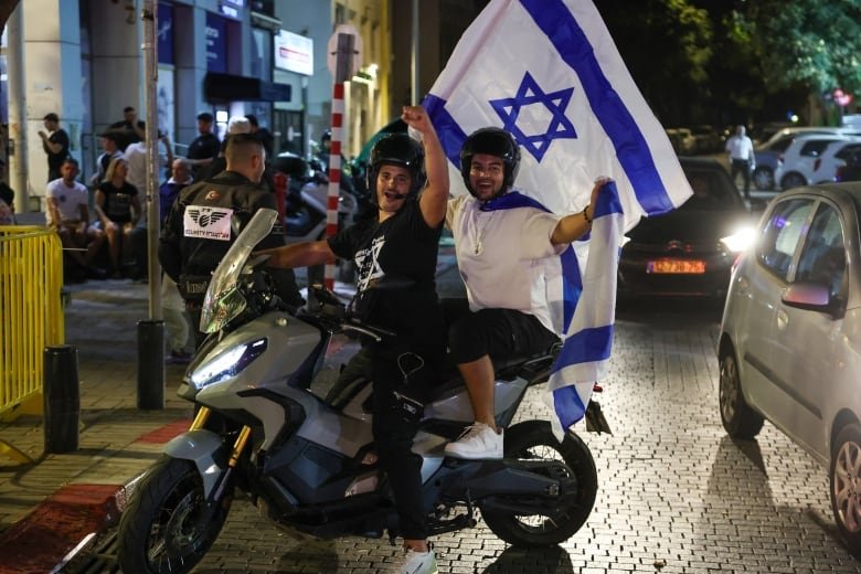 Smiling men on motorcycles wave an israeli flag