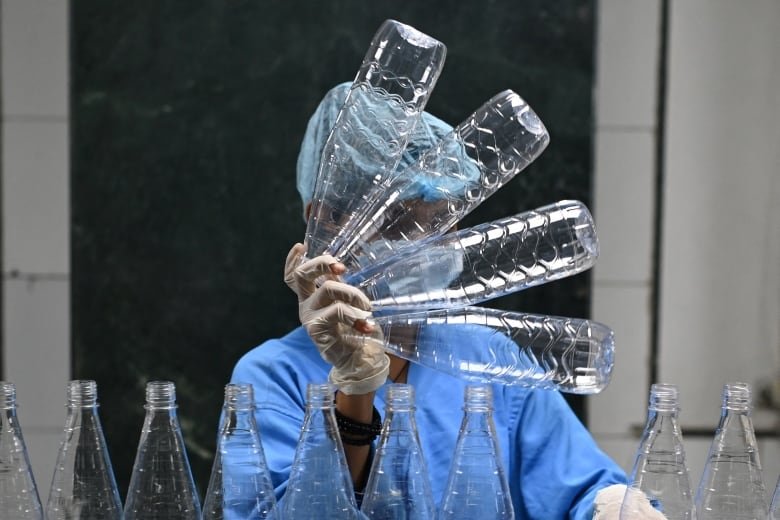 A worker holds up 4 plastic bottles at a bottling plant in Manesar, India.