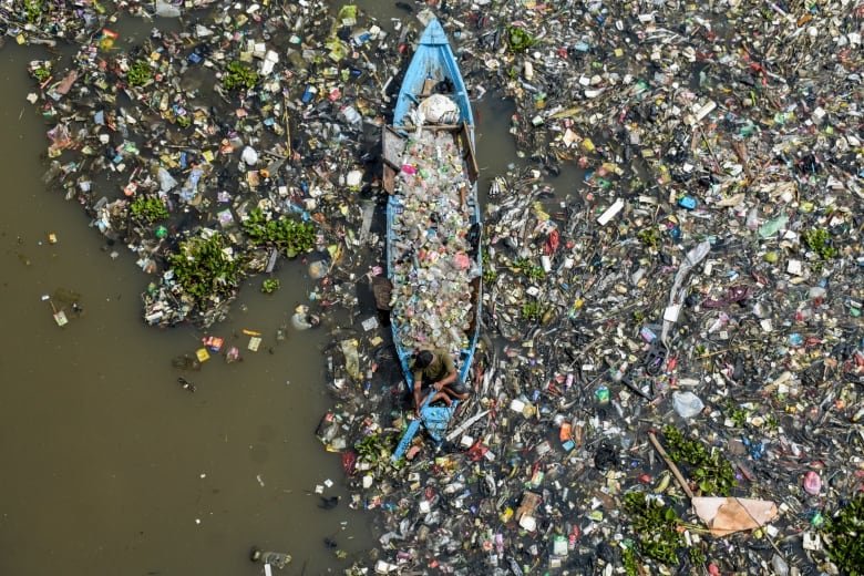 A man on a boat collects recyclable plastics from the heavily polluted Citarum River at Batujajar in Bandung, Indonesia.