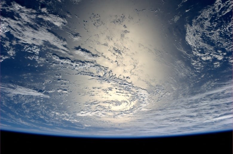 About one sixth of the Earth is visible in space. Clouds and blue are visible on the Earth, as well as a large area centred in the photo filled with glare.