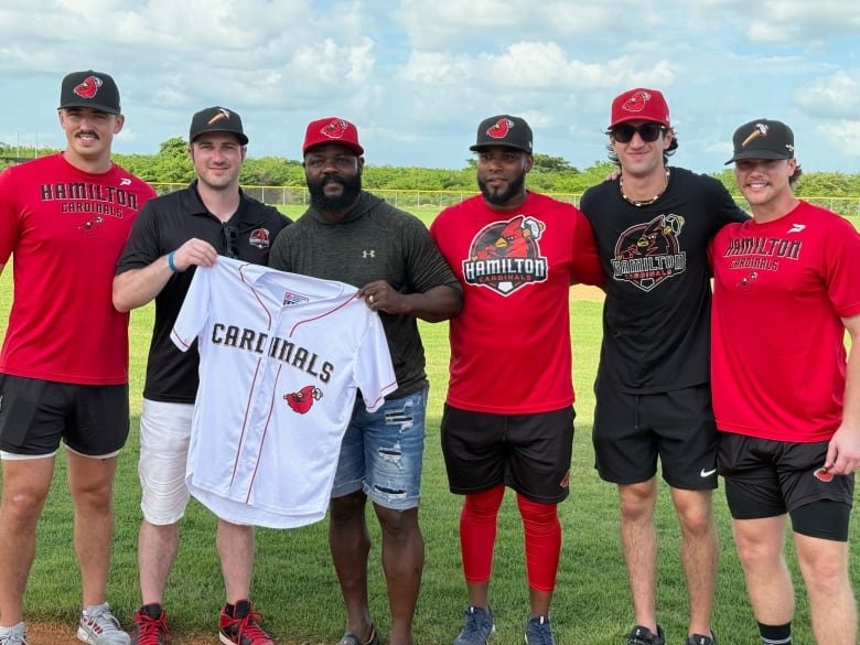 Six people stand holding up a Cardinals jersey.