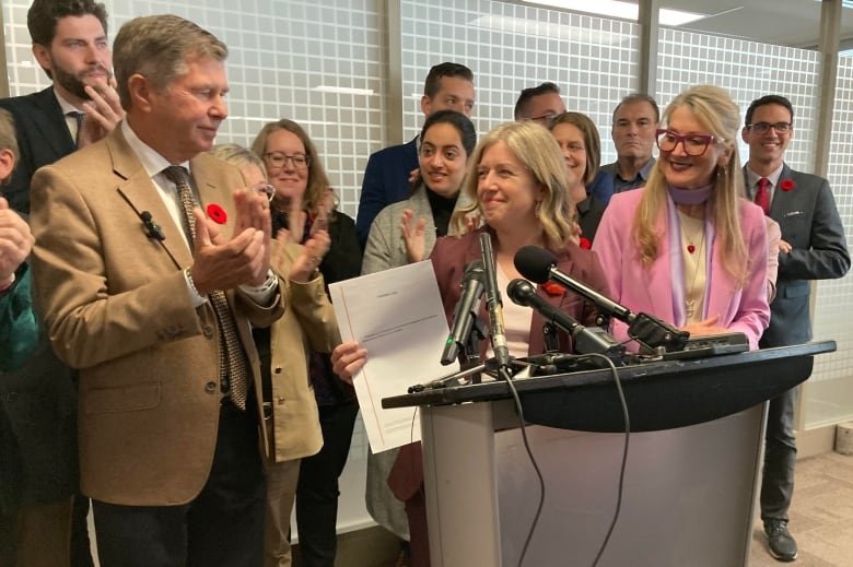 A group of people stand behind a microphone. One of them is holding up a document.