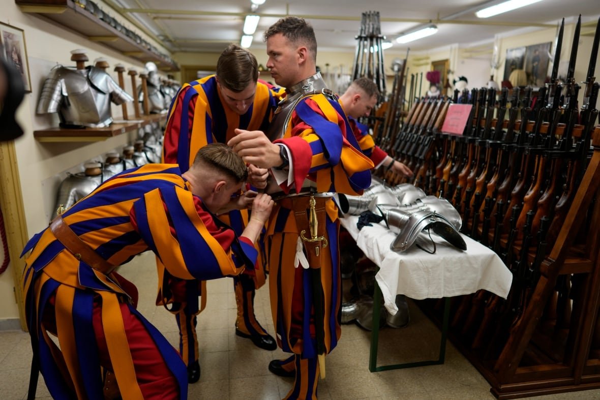 Two men in striped coloured outfits assist a third man with his outfit.