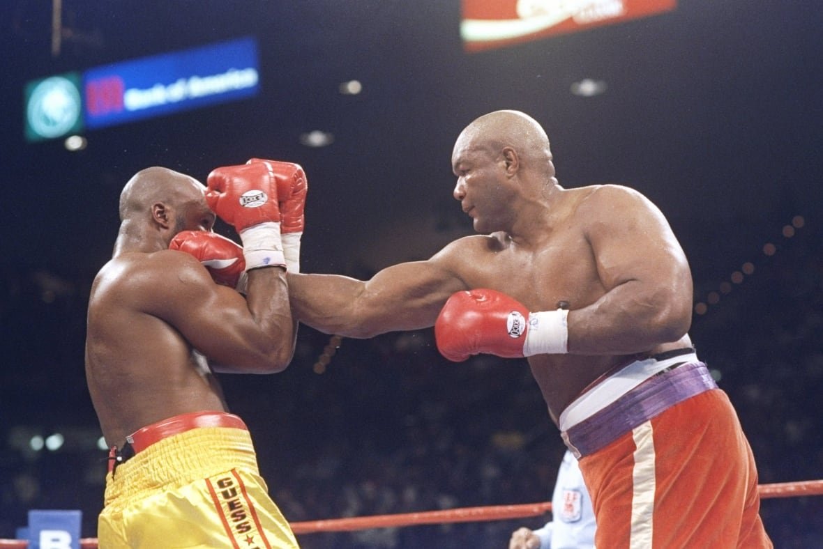 1398163 Two large, dark complected bald men are shown in a boxing ring. The fighter with red and blue trunks throws his right glove between the guard of the figther in yellow shorts.