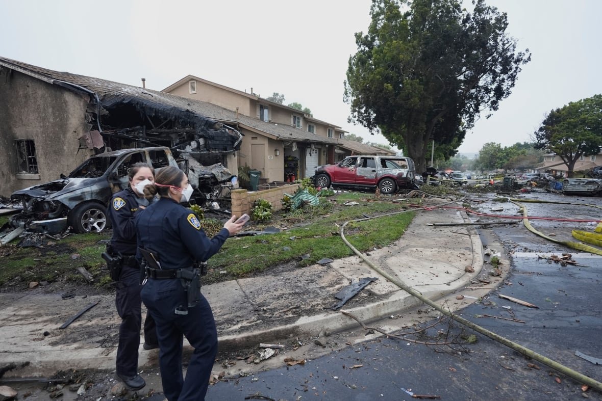 aptopix-plane-crash-san-diego Two female officers standing at the corner of a residential street where a plane crash occurred leaving a 'debris field.'