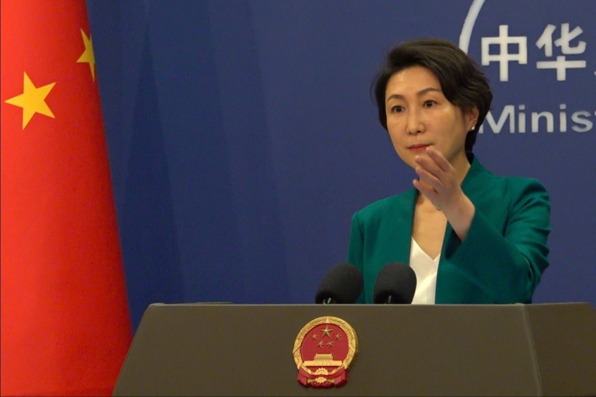 An Asian woman gestures with her hand while speaking at a podium and wearing a green blazer.