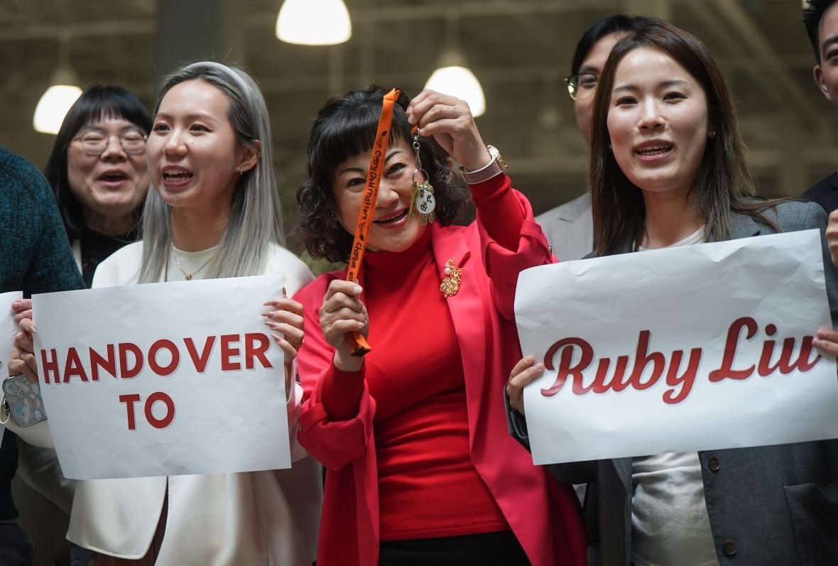 hudsons-bay-ccaa-20250626-ruby-liu A group of people smile. Two of them are holding up signs reading 'handover to Ruby Liu'.