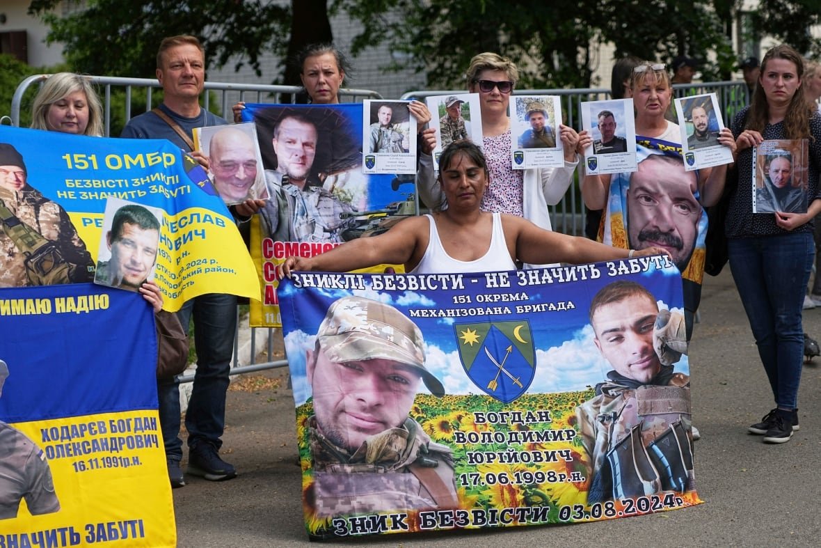 russia-ukraine-war-prisoners Several people, men and women, stand on the pavement holding up signs or banners.