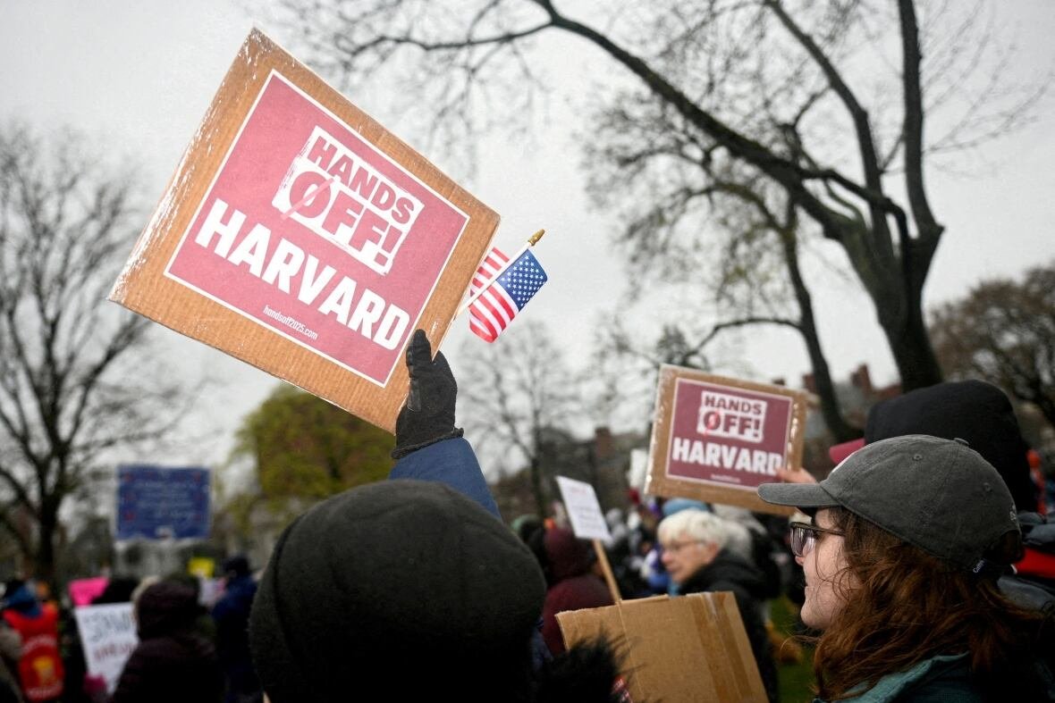 Signs and people are shown at an outdoor demonstration. One sign says 'Hands off Harvard.'