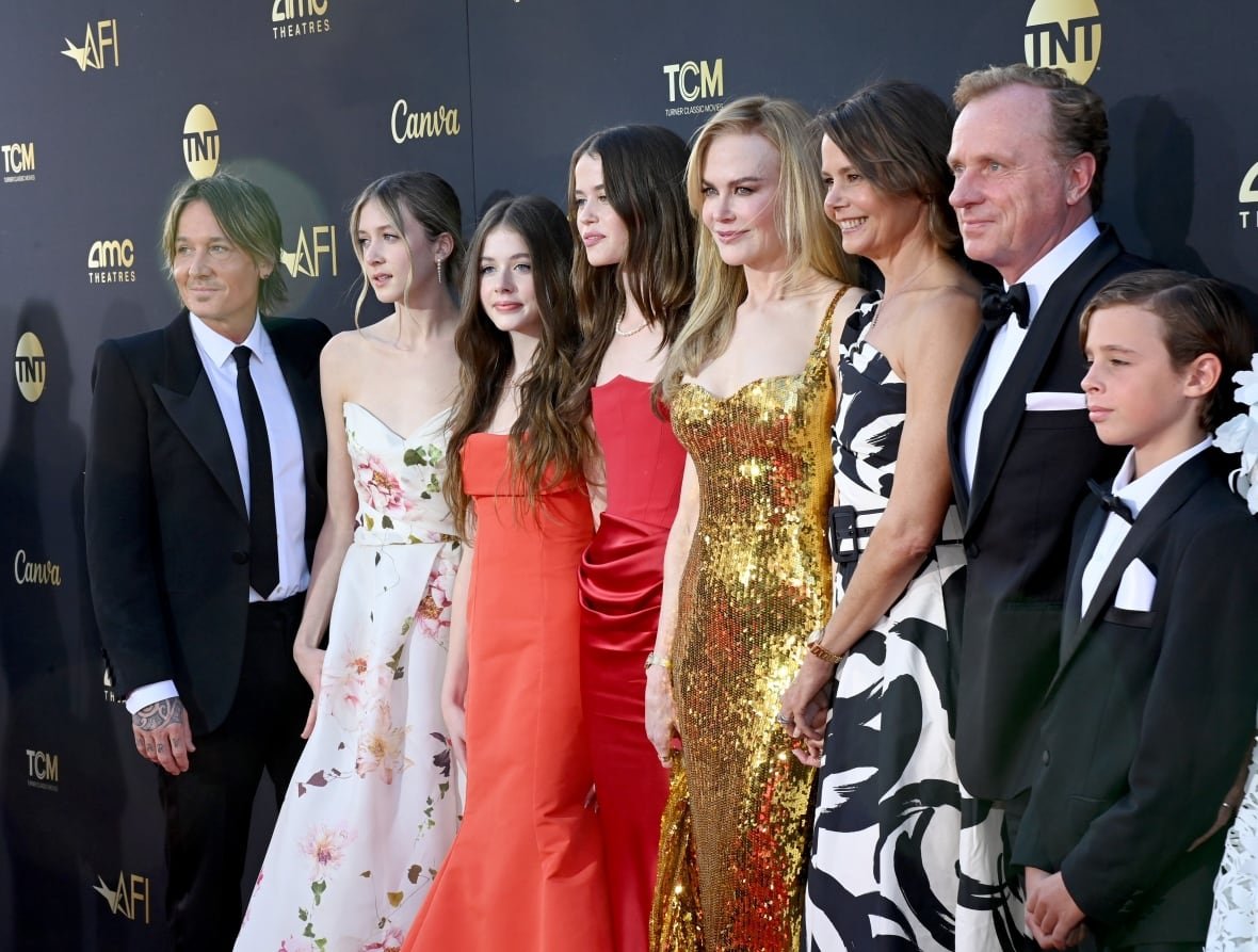 keith-urban-nicole-kidman-family-april-2024 A family in formal wear, men and boys in black suits and ties and women and girls in gowns, pose for a photo in front of a black backdrop.