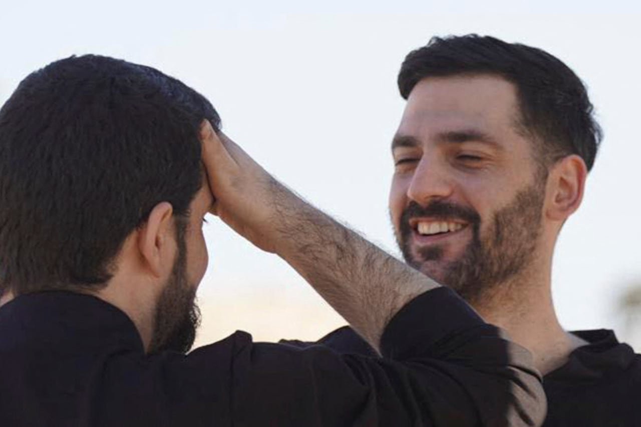 Two men in black shirts facing one another, one man is smiling.