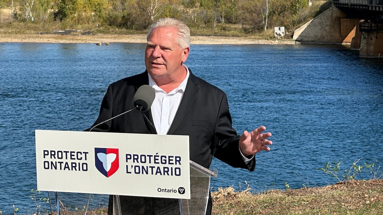 Elderly man speaking at a podium with a "Protect Ontario" sign