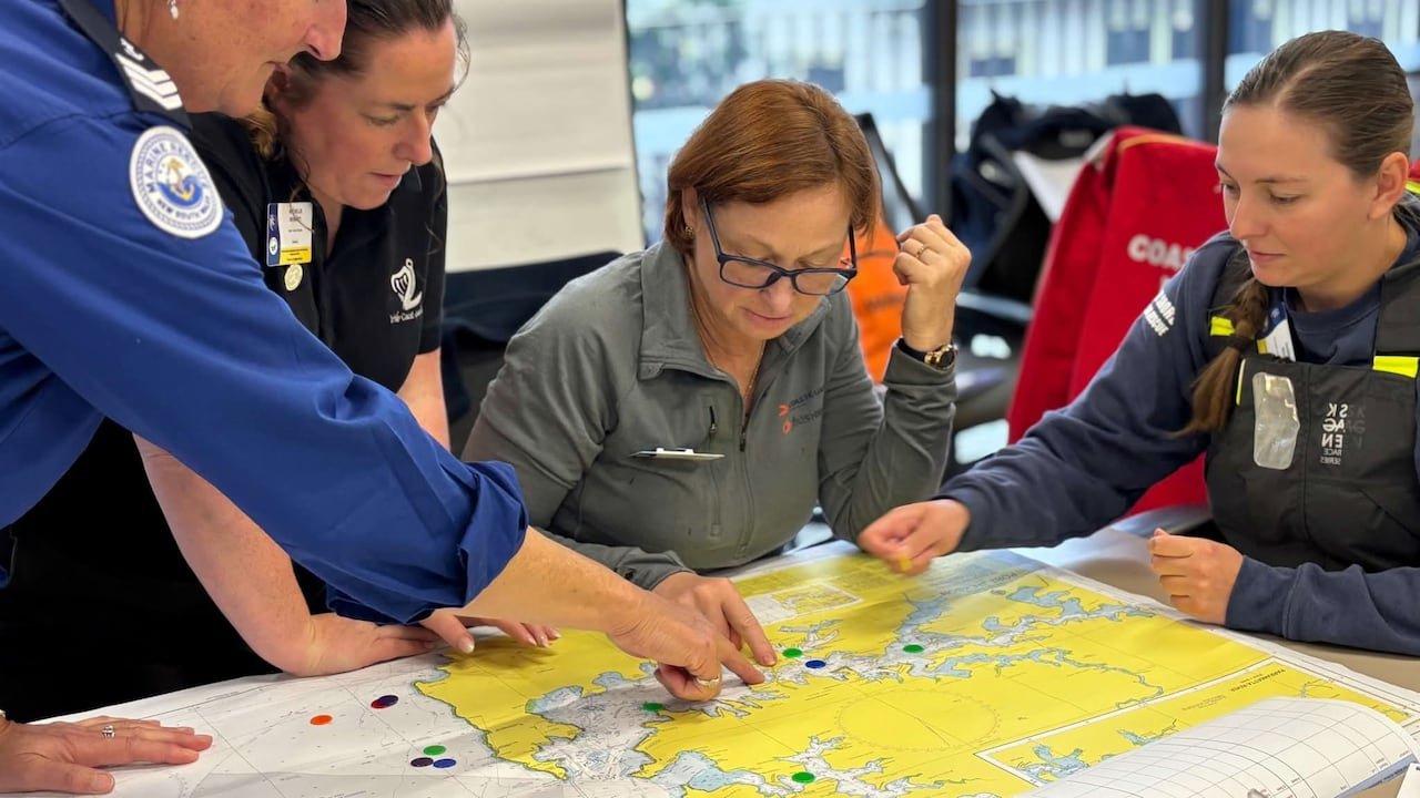 Four people stand around a table pointing at a map.