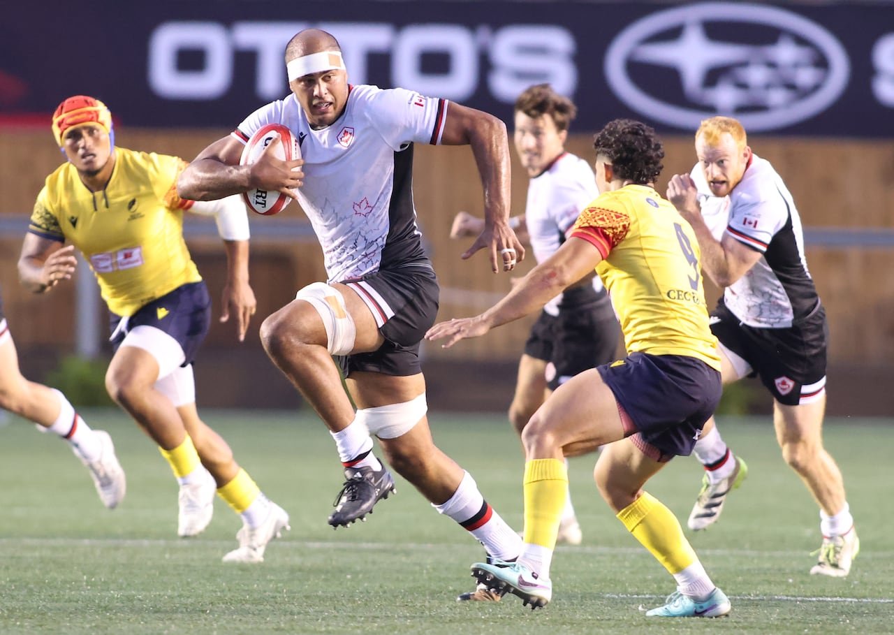 A rugby player in a white Canadian uniform avoids an opponent in a yellow Romanian uniform.
