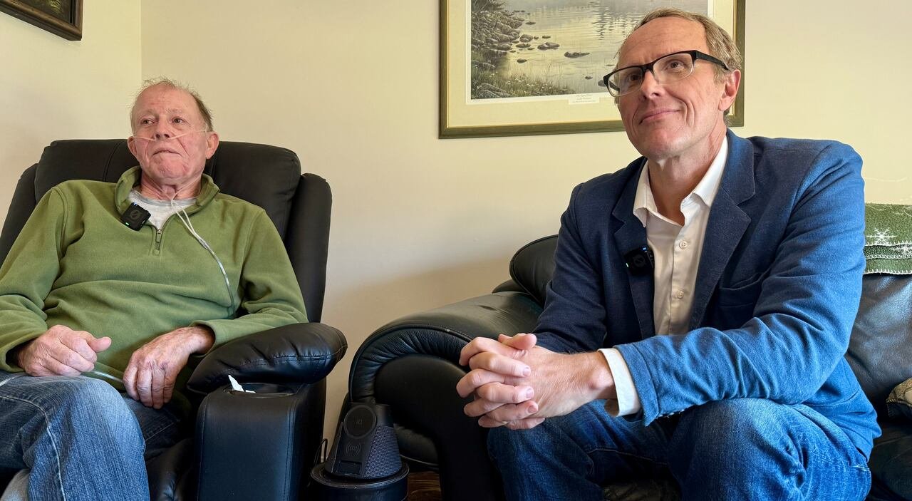 A man in a green sweater sits next to a man in a blue blazer.