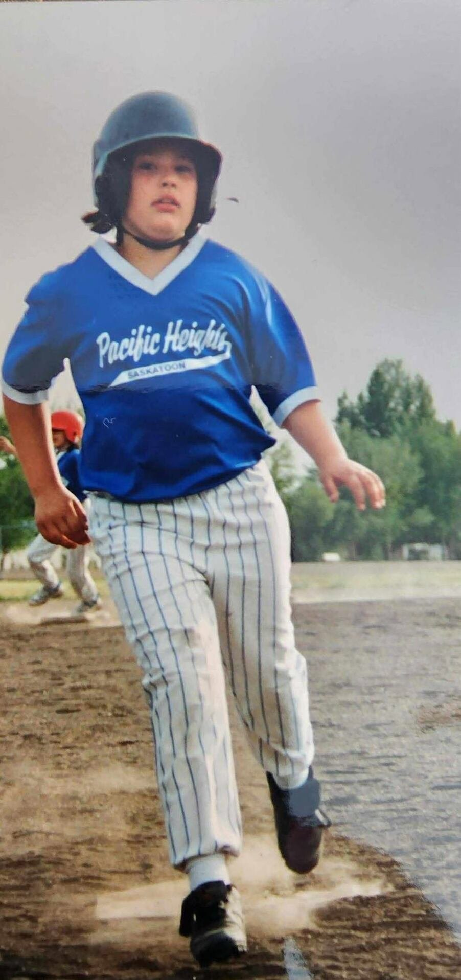 A child in a baseball uniform and batting helmet runs on a field.