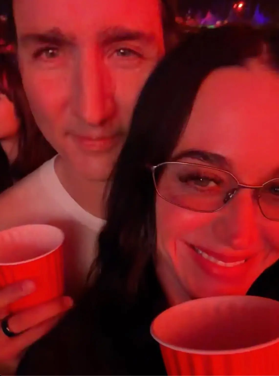 A couple taking a selfie at a concert, holding drinks and smiling.