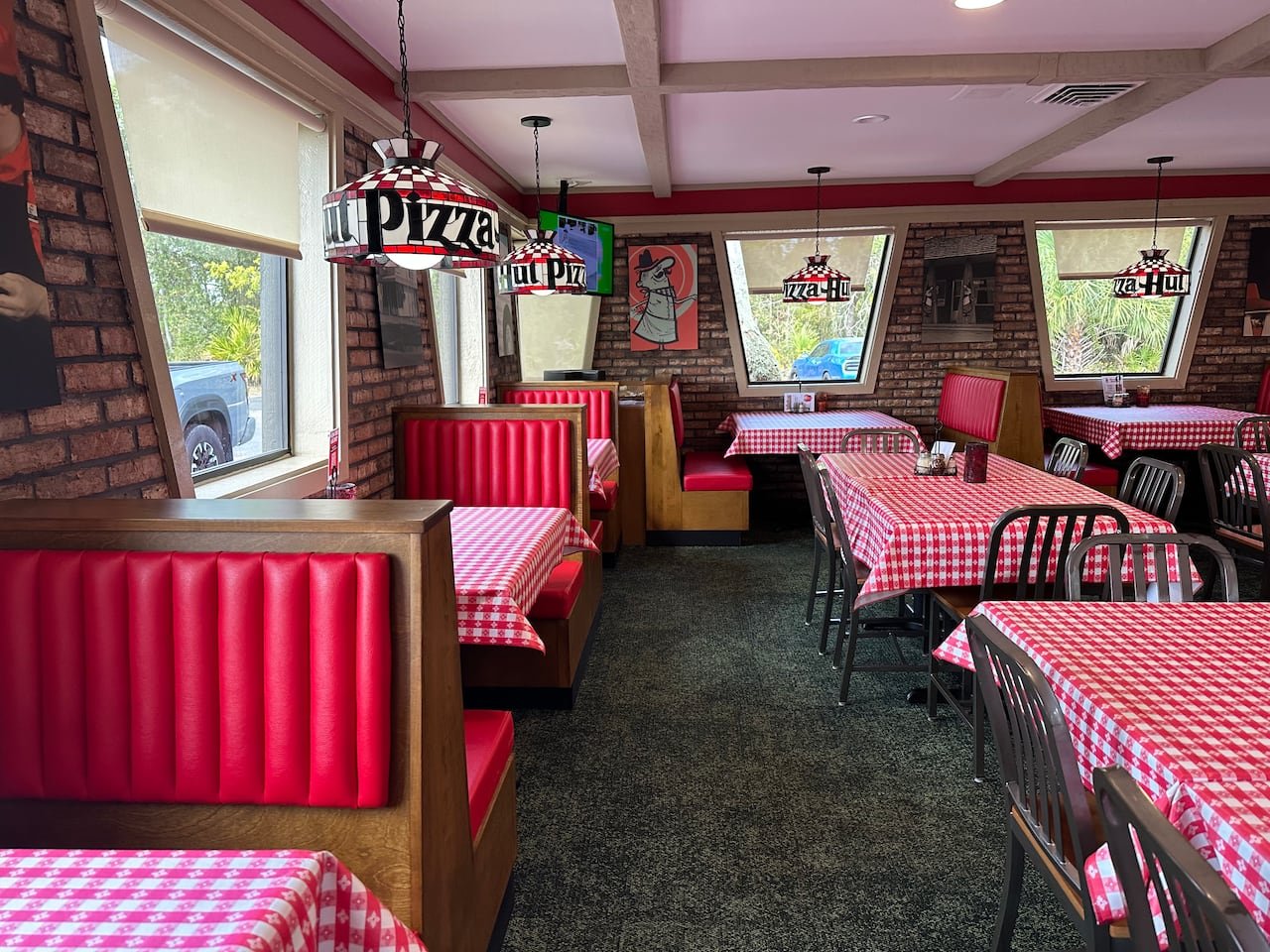 A classic Pizza Hut location with red checkered tablecloths, red booths, and stained glass lamps