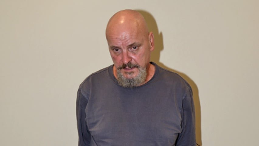 A man in a blue shirt against a pale-colored wall.