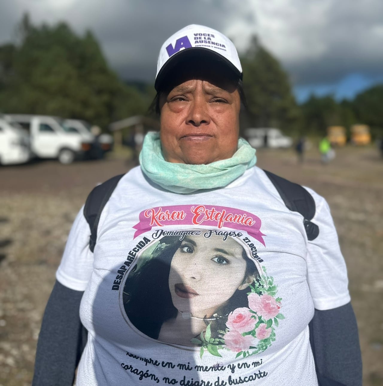 A woman with a white shirt with the photo of her daughter looks into the camera.