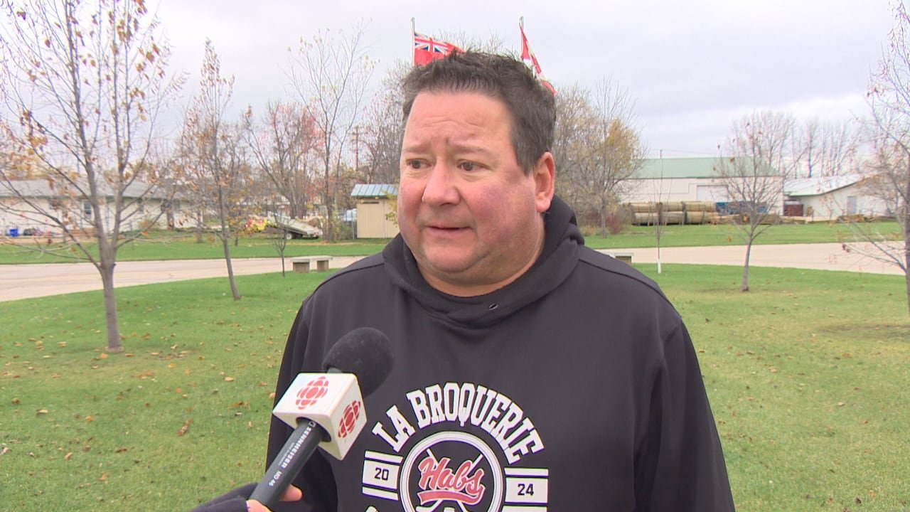 A man with a black, white, and red sweater speaking into a microphone