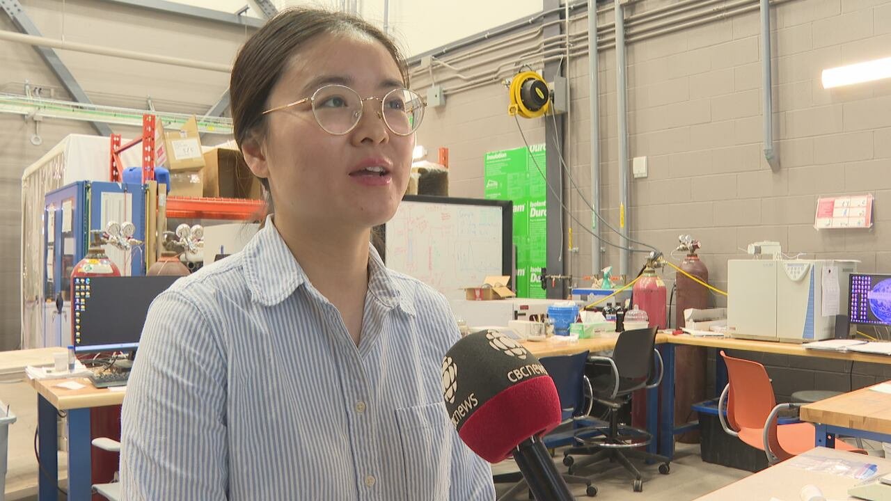 default-486 A woman in glasses and a button up stripped shirt speaks into a CBC microphone. She is standing in front of a lab.