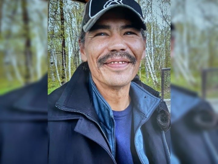 Man with baseball cap smiles in a blue sweater and jacket.
