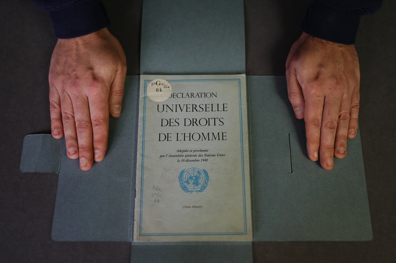 default-991 Two hands beside a copy of an old document titled "Declaration Universelle des Droits de l'Homme" (Universal Declaration of Human Rights).