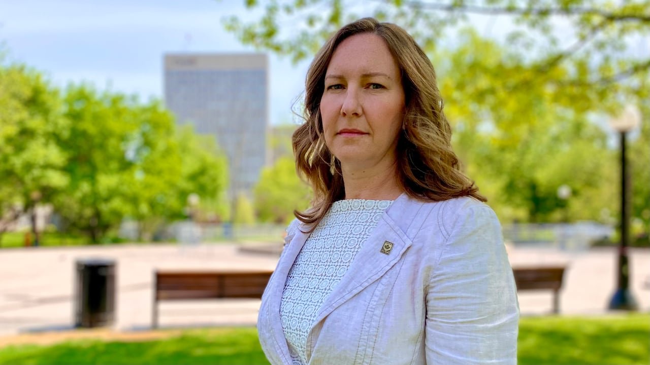 A woman in a suit jacket stands in a park.