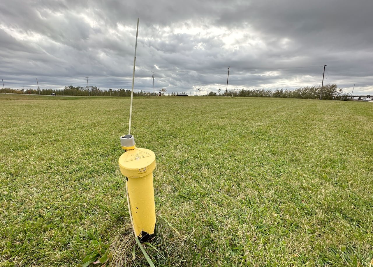 A yellow metal pipe with a metal cap on it and a metal pole sticking out the top is seen in the middle of a field of green grass.
